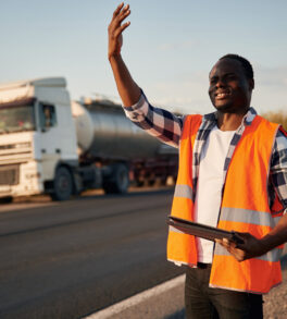 Showing the way. Black man is standing on the road with truck on it.